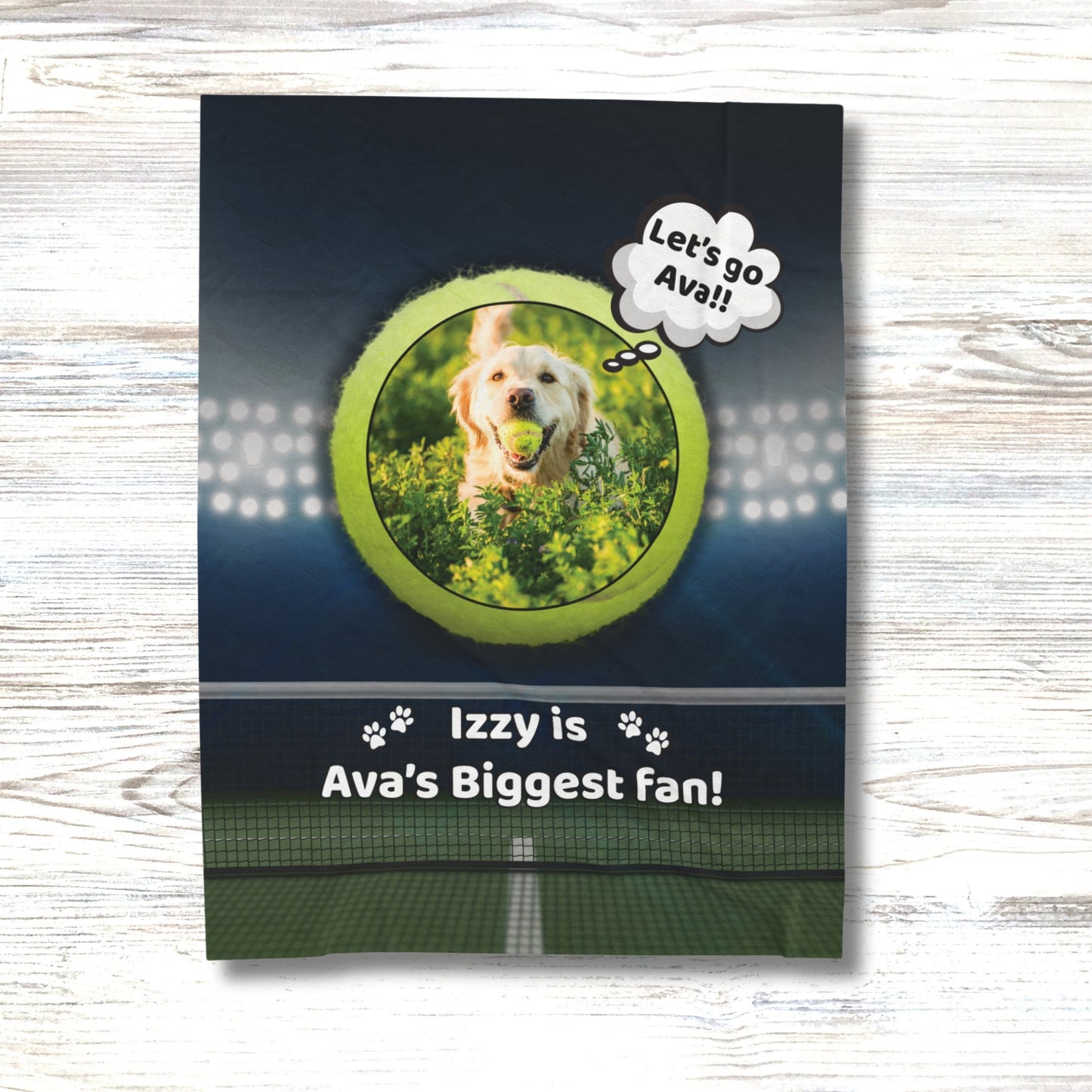 Personalized dog blanket on a white wood background, featuring a golden retriever with a tennis ball inside a green tennis ball frame, with the phrase “Izzy is Ava’s Biggest Fan!” and stadium lights above a tennis court.