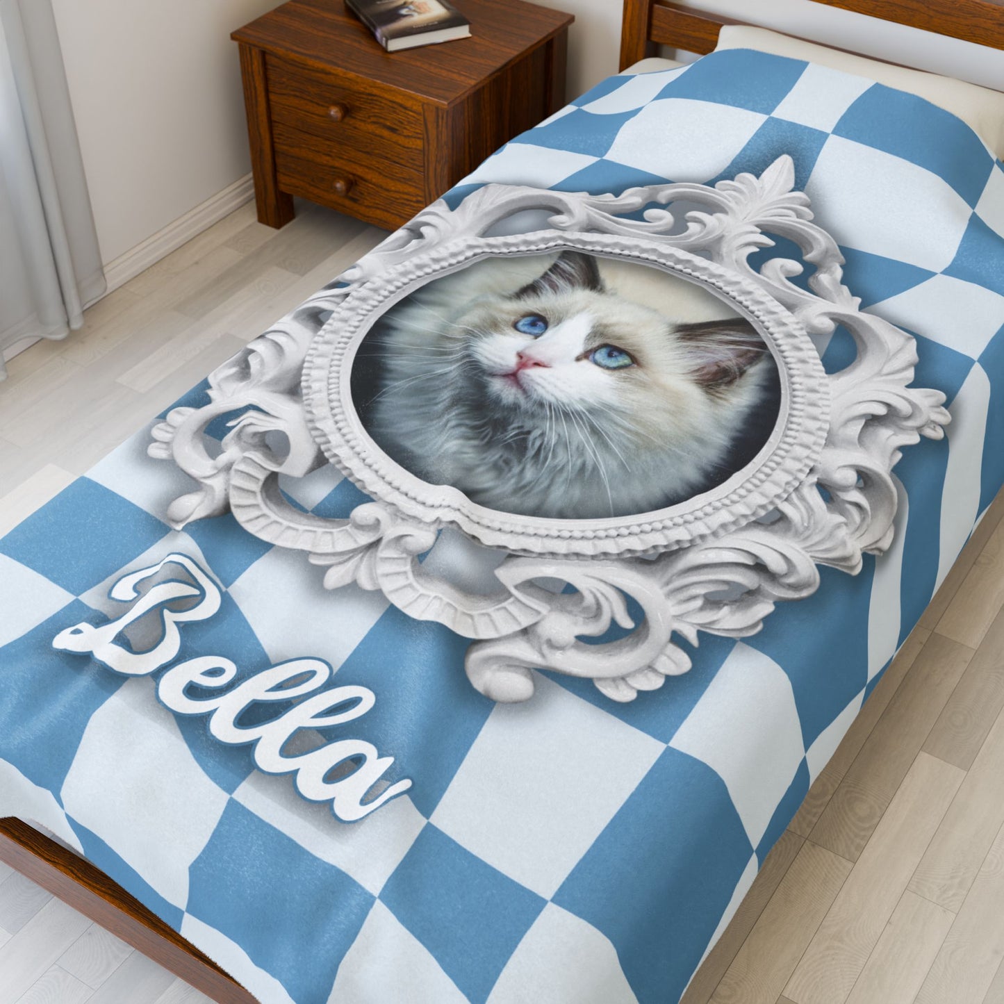 Close-up view of personalized cat blanket featuring ornate white frame and pet name "Bella" displayed on a checkered blue bed