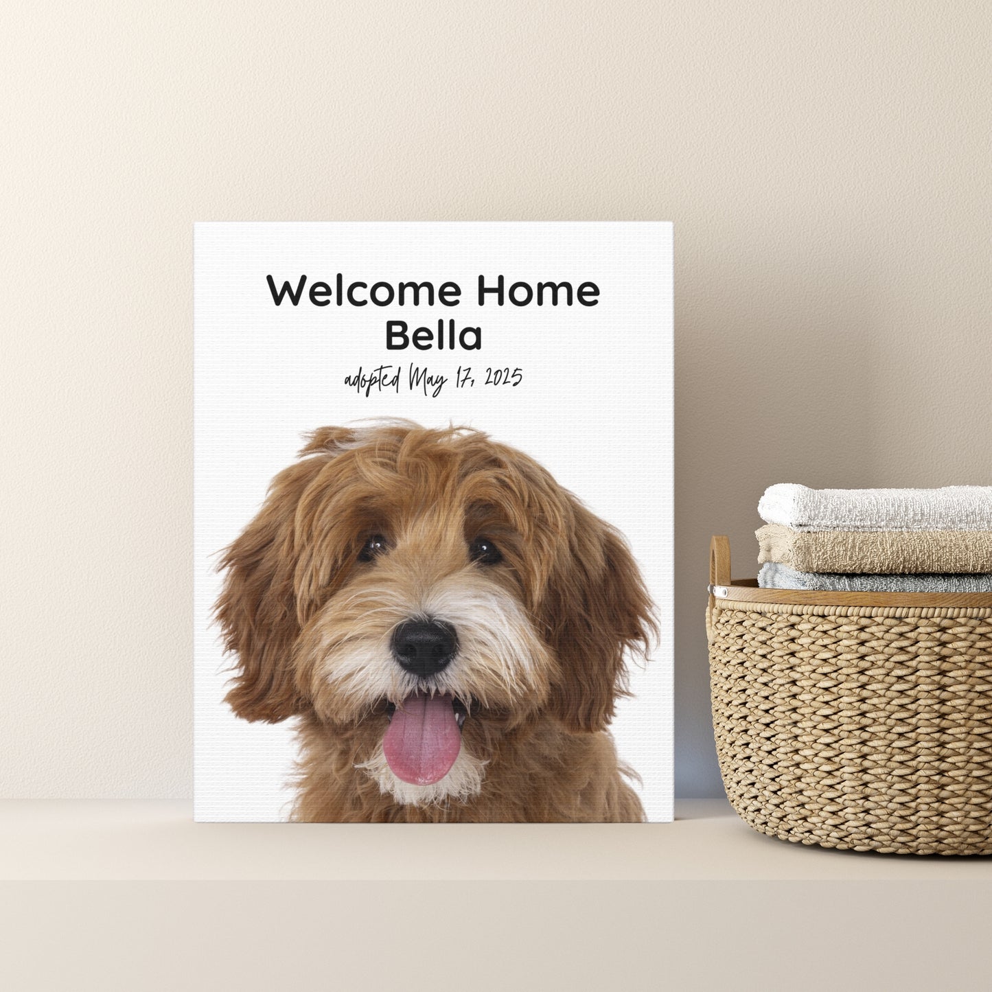 Personalized dog adoption canvas print featuring a brown doodle and the name Bella, displayed on a shelf beside a woven basket and folded towels.