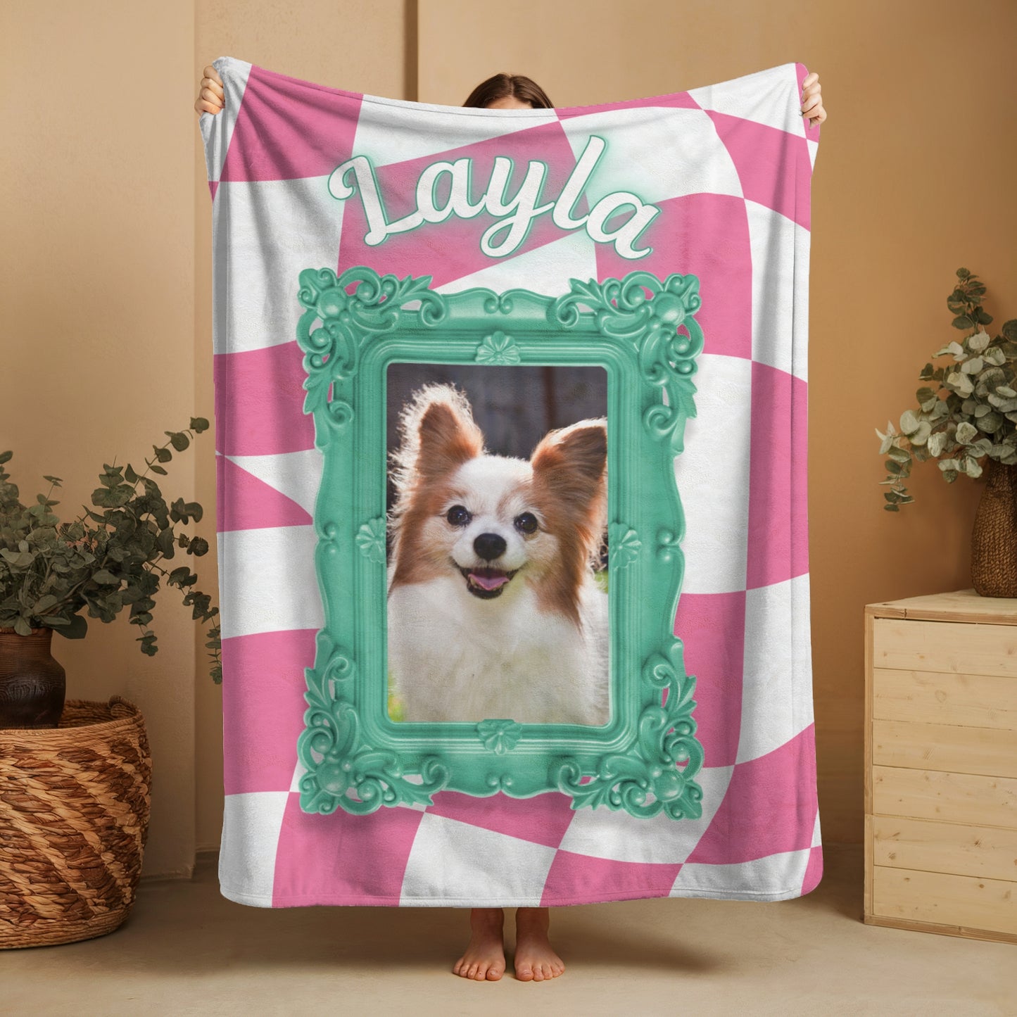 Young woman holding a personalized pink and green dog blanket featuring the name Layla and a framed photo of a dog