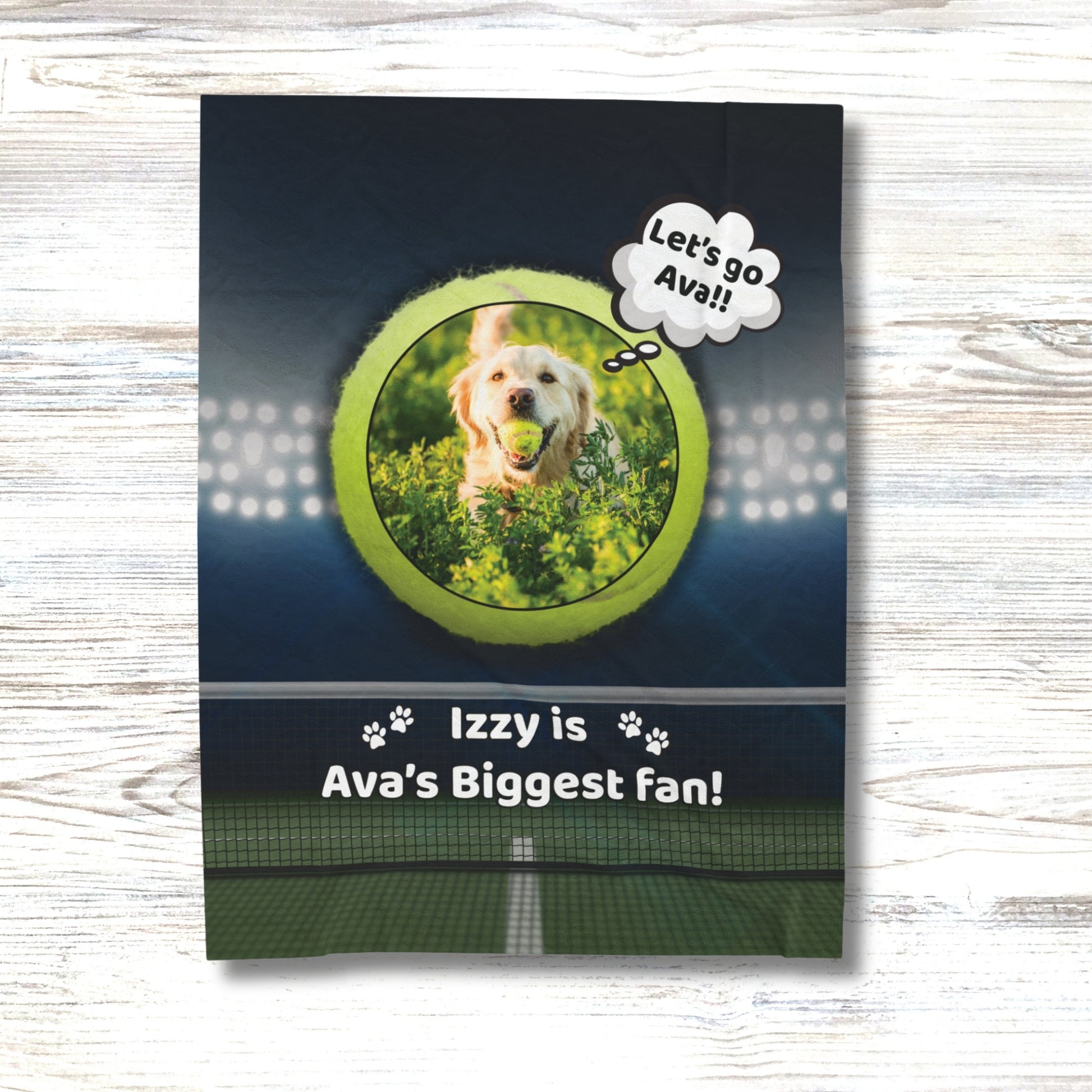 Personalized dog blanket on a white wood background, featuring a golden retriever with a tennis ball inside a green tennis ball frame, with the phrase “Izzy is Ava’s Biggest Fan!” and stadium lights above a tennis court.