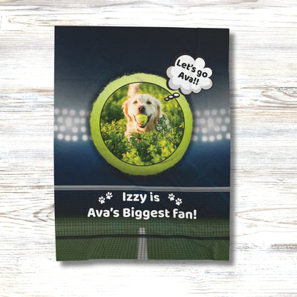 Personalized dog blanket on a white wood background, featuring a golden retriever with a tennis ball inside a green tennis ball frame, with the phrase “Izzy is Ava’s Biggest Fan!” and stadium lights above a tennis court.