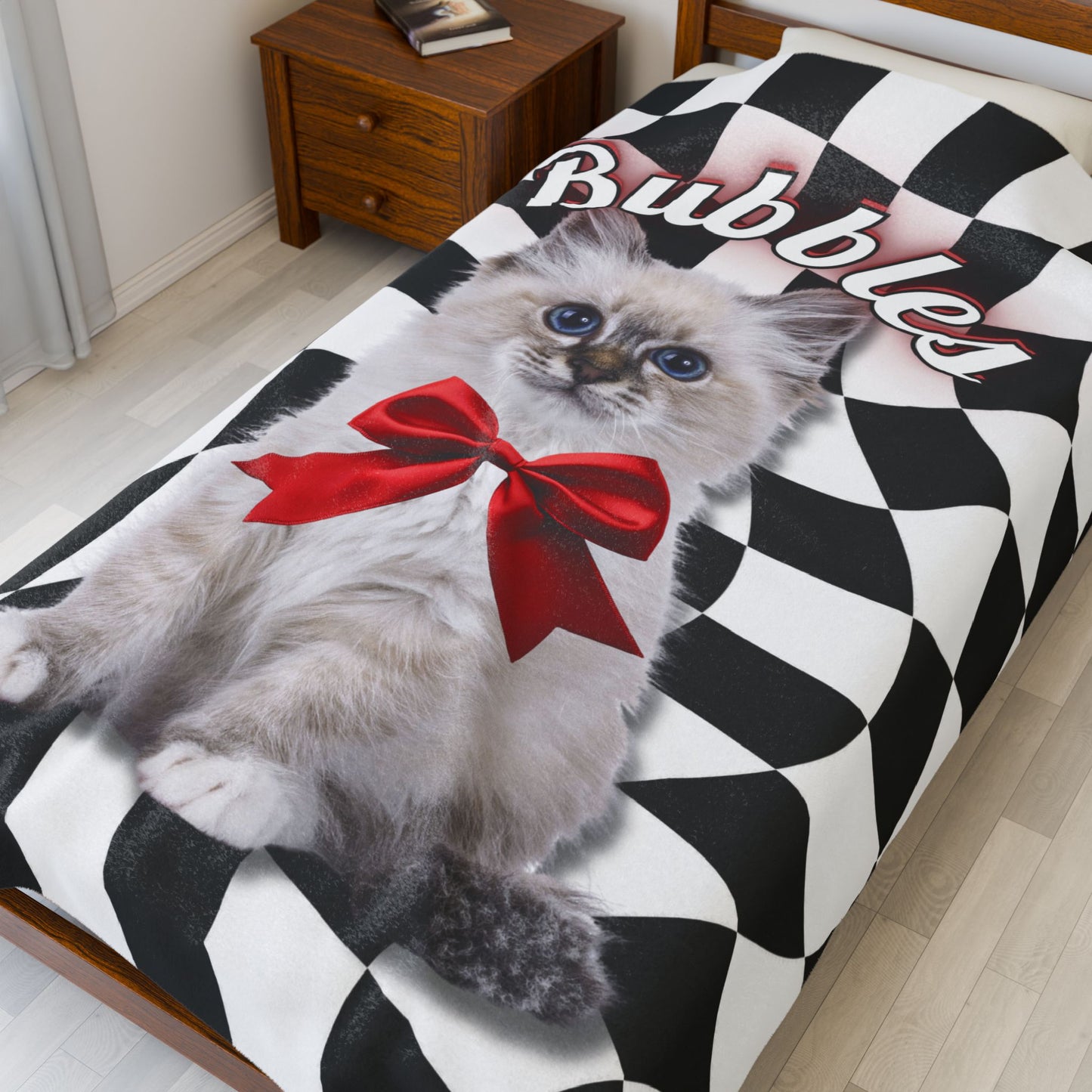Personalized cat blanket featuring a kitten named Bubbles with a red bow, shown on a bed with a black and white checkered swirl background